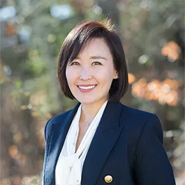 A woman with brown hair. She is wearing a blue blazer and a white blouse.