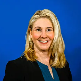 A woman with shoulder length hair with blond highlights. She is wearing a black blazer and a green blouse.